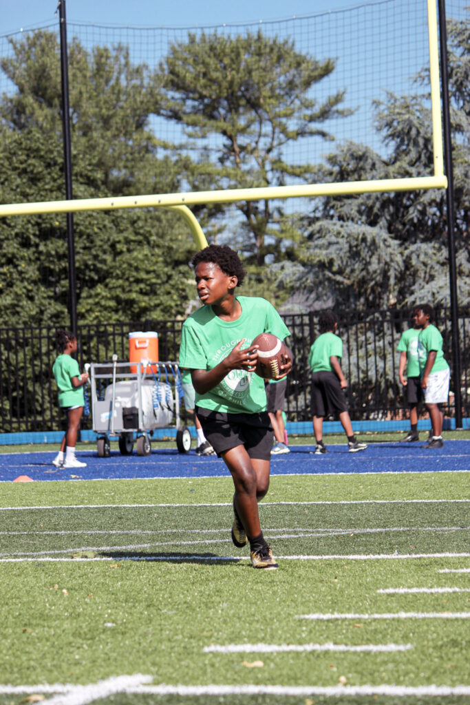 Young teenager holding a football and running on a football field